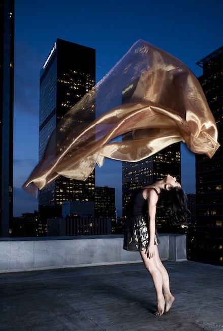 Jessica Chen on the top of a building with a flowing scarf surrounded by the lights of the city